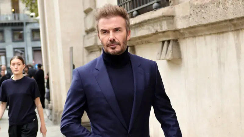 David Beckham luce un elegante traje azul con jersey de cuello alto, caminando con confianza.