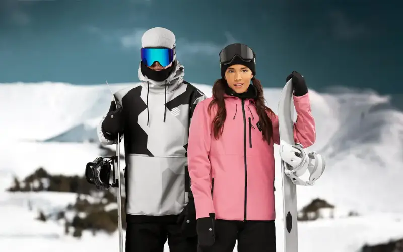 Pareja con tablas de snowboard, ella con chaqueta rosa, él con chaqueta gris y negra. Opiniones sobre Sorona Aura: ¡calidez y estilo en la montaña!